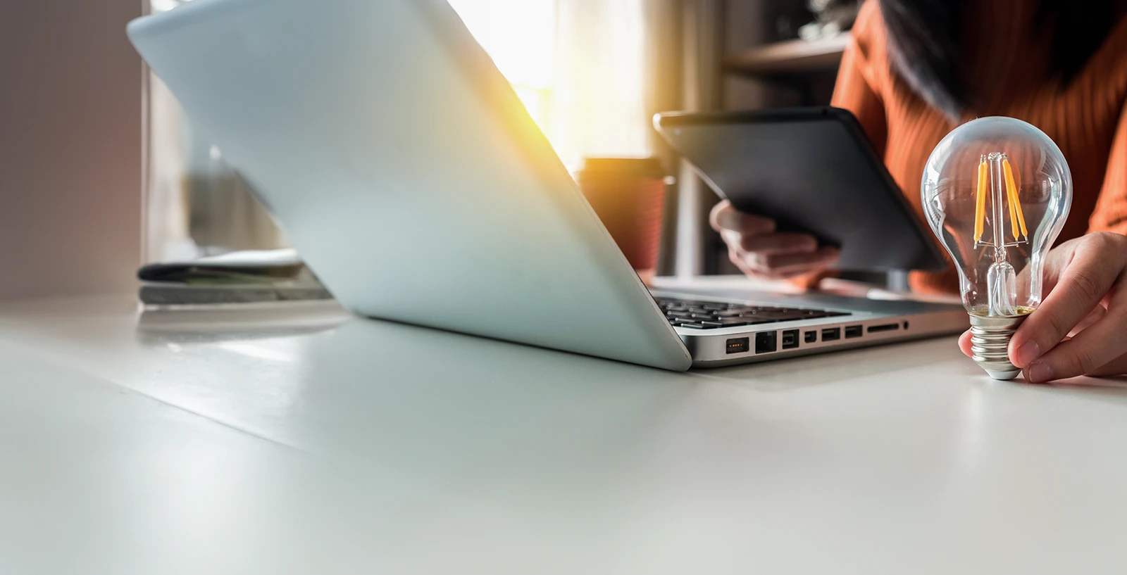 person viewing their phone in front of a laptop, holding a lightbulb to represent lightbulb moments