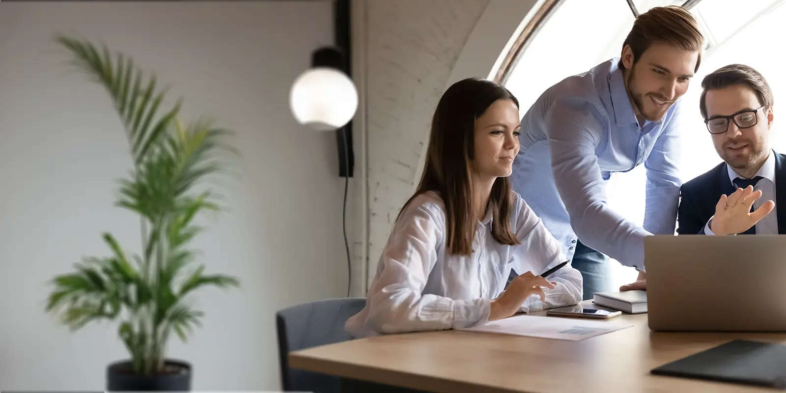 Three people in a meeting room with a laptop
