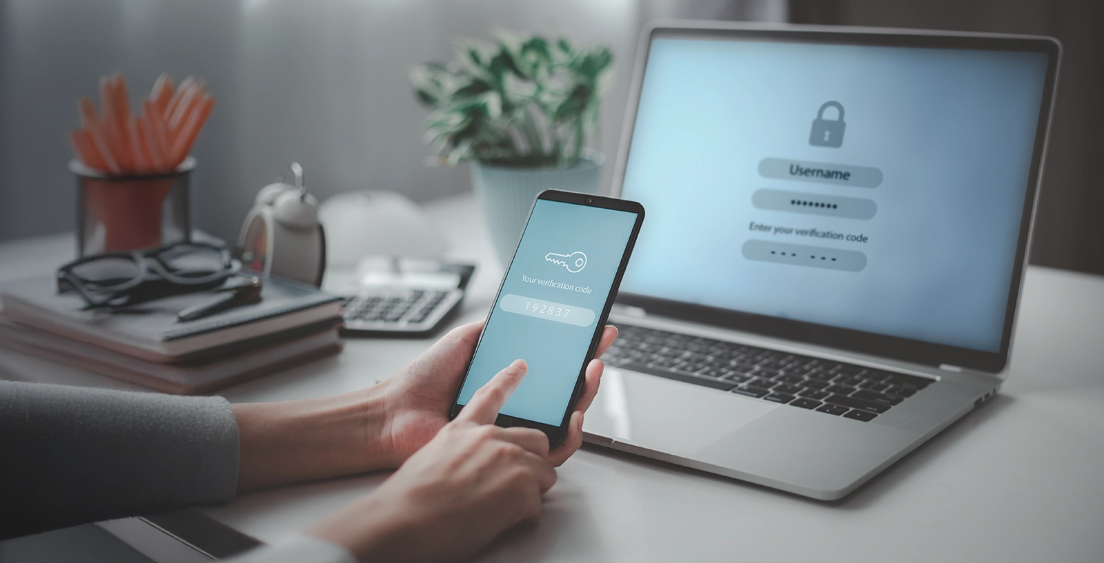 A person holds a smartphone showing a verification code while logging in on a laptop using two-factor authentication.