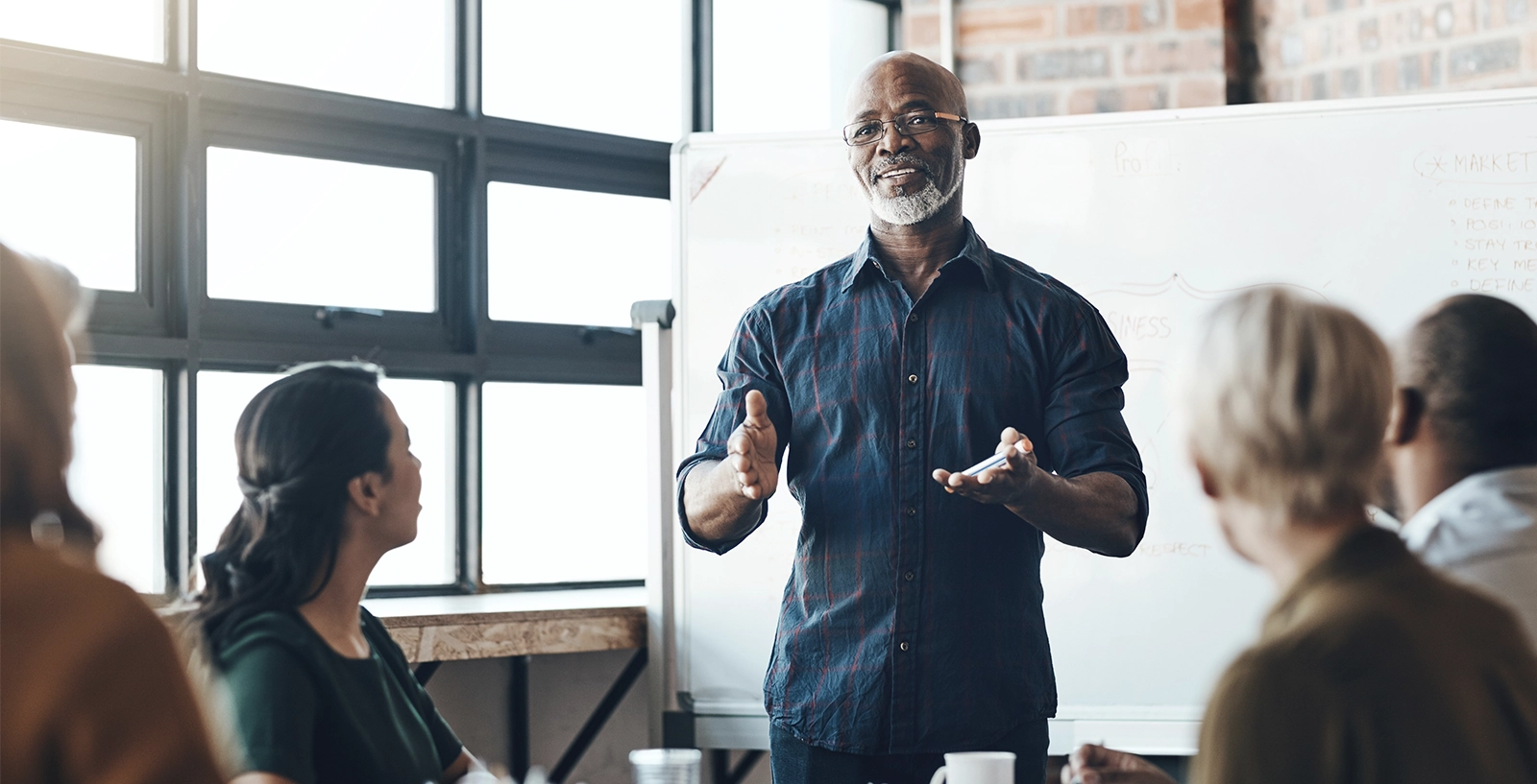 Person presenting to a group in a bright office meeting room with a whiteboard in the background