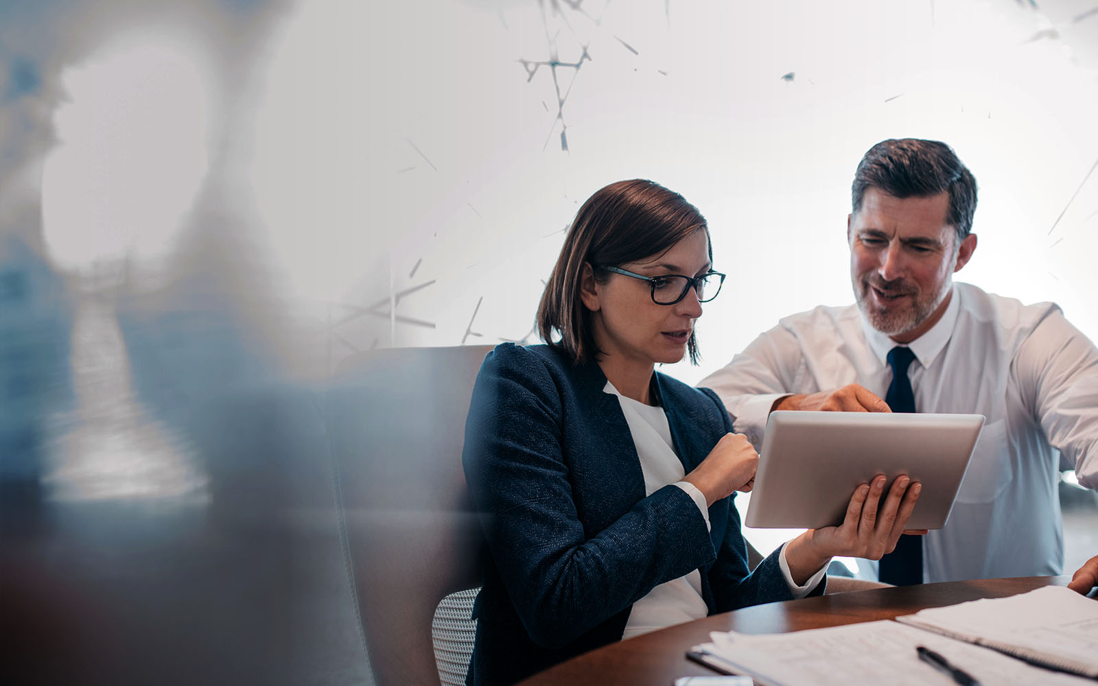Two confident business people working on a  tablet together while working at a table in a modern off