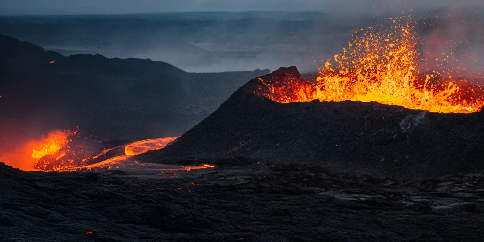 Volcanic eruption with bright lava and rocky terrain.