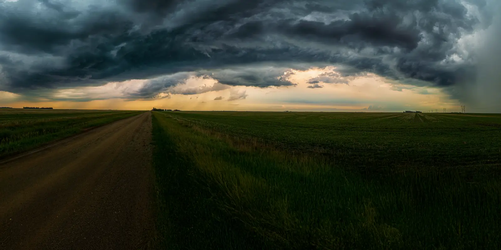 Storm clouds over open field with dirt road.