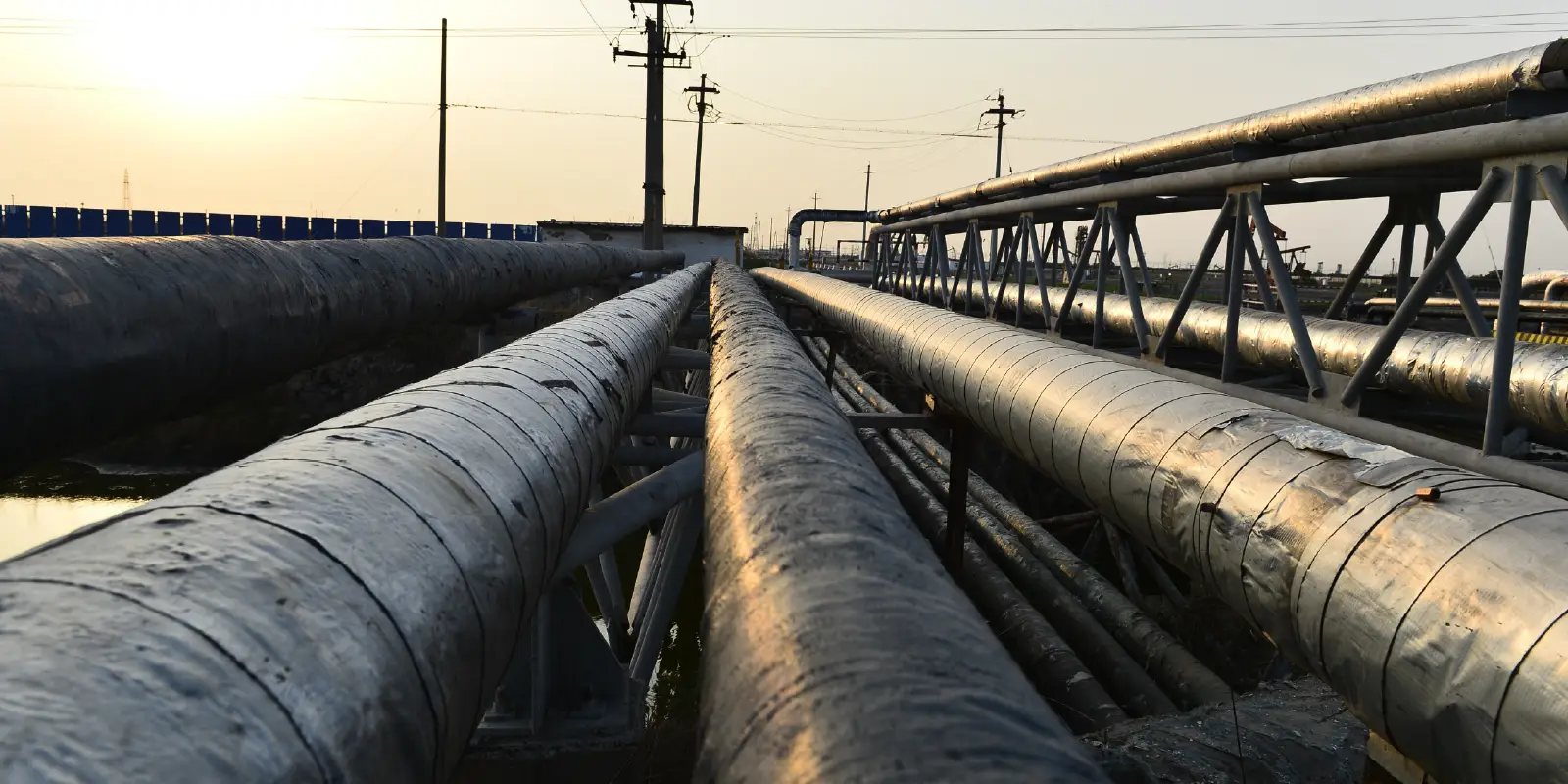 Industrial pipelines at sunset with power lines.