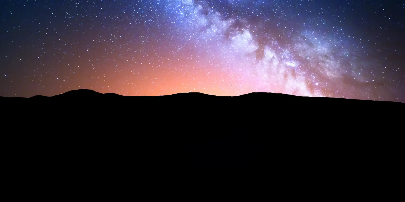 Starry night sky with Milky Way over mountains.