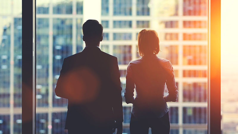 Businessman and businesswoman staring out of a window of a boardroom