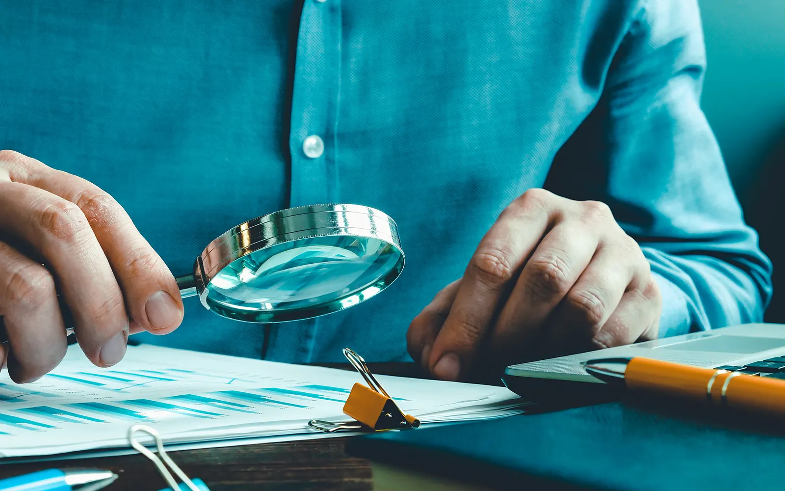 Hands holding a magnifying glass over a document