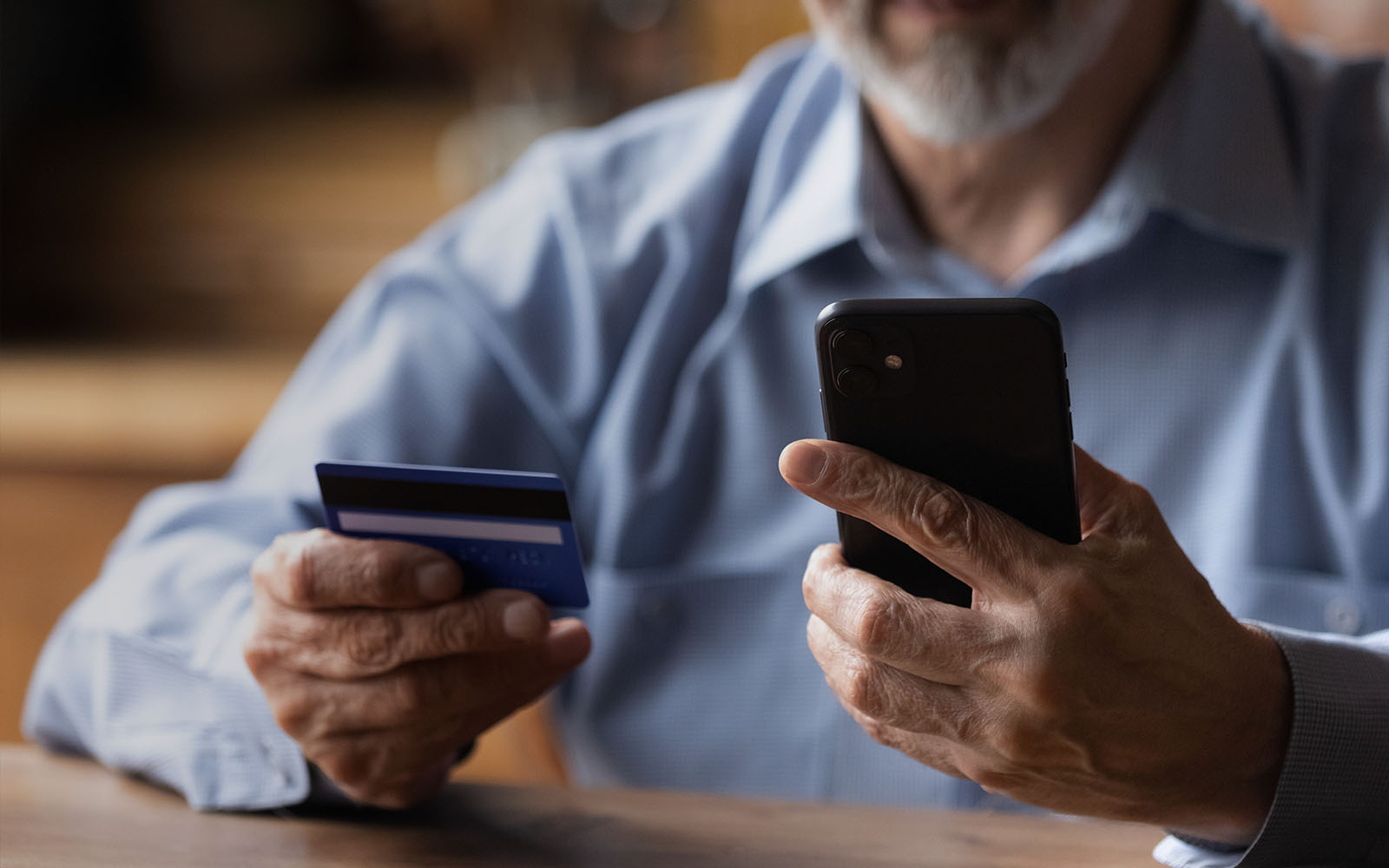 mature man using phone, holding credit card