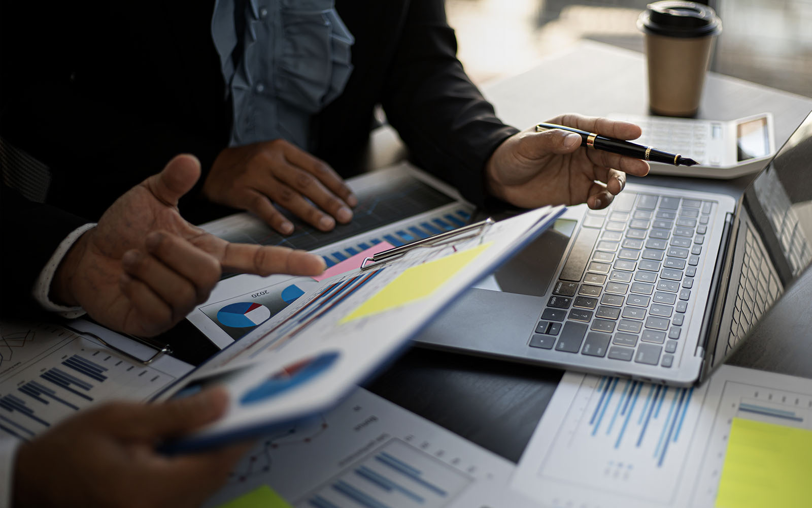 Two pairs of hands pointing to graphs and laptop