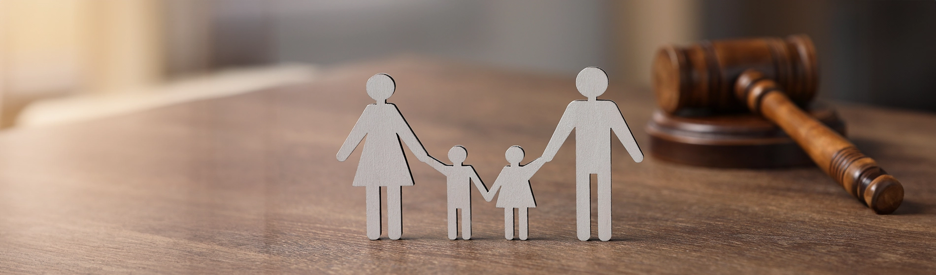 Wooden family figures holding hands with a gavel in the background on a wooden table.