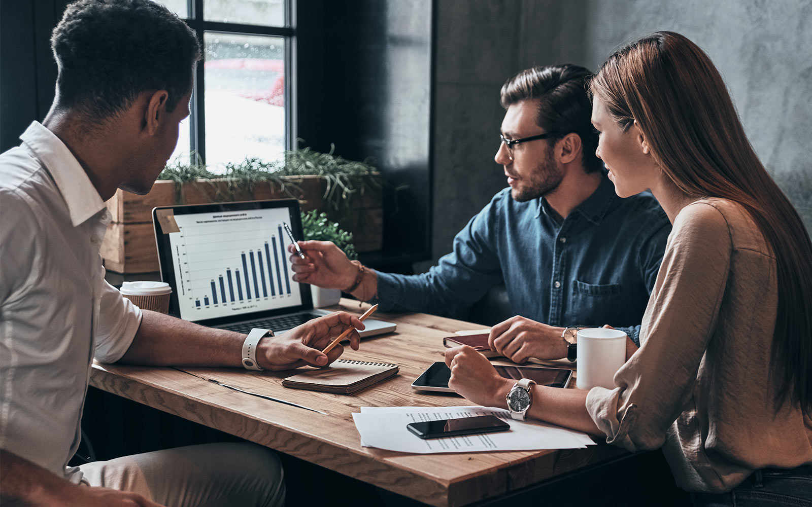 Three people sitting at a table discussing a bar graph on a computer screen