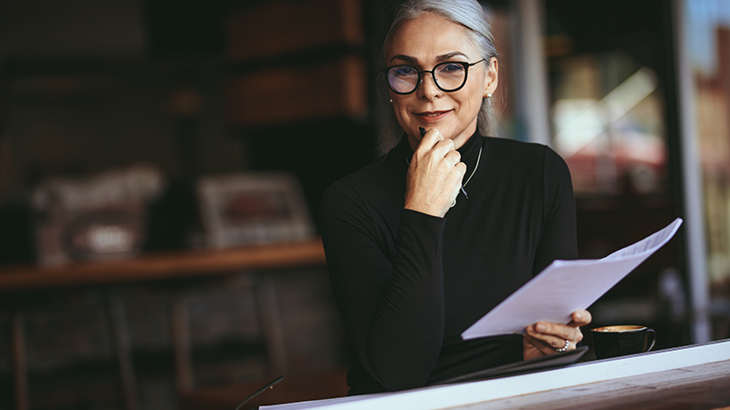 Femme souriante et tenant des papiers dans une main et un stylo dans l'autre