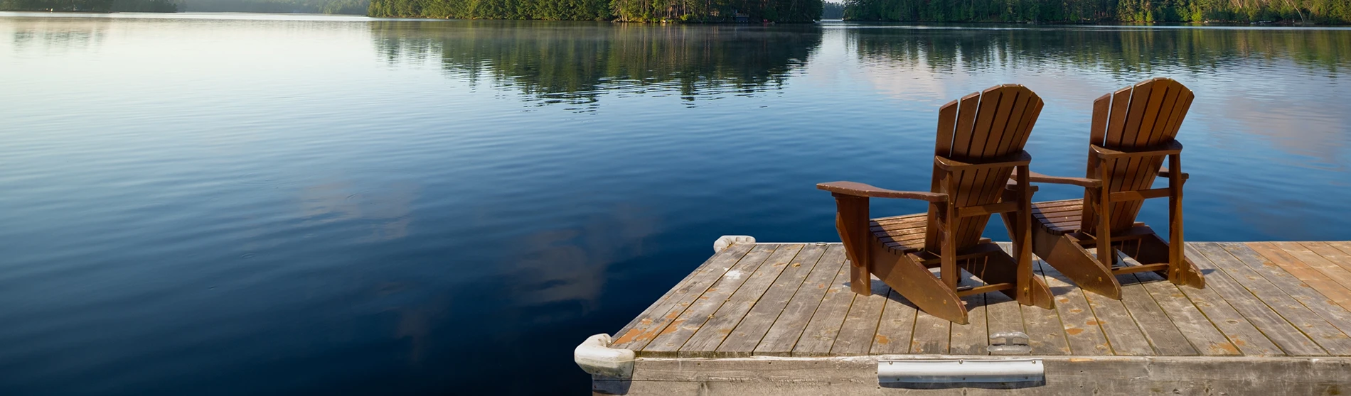 Two Adirondack chairs sit on a wooden dock