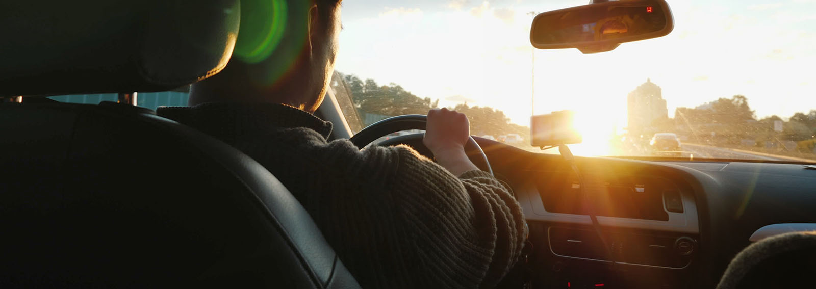 Man driving a car with the setting sun in the windshield.