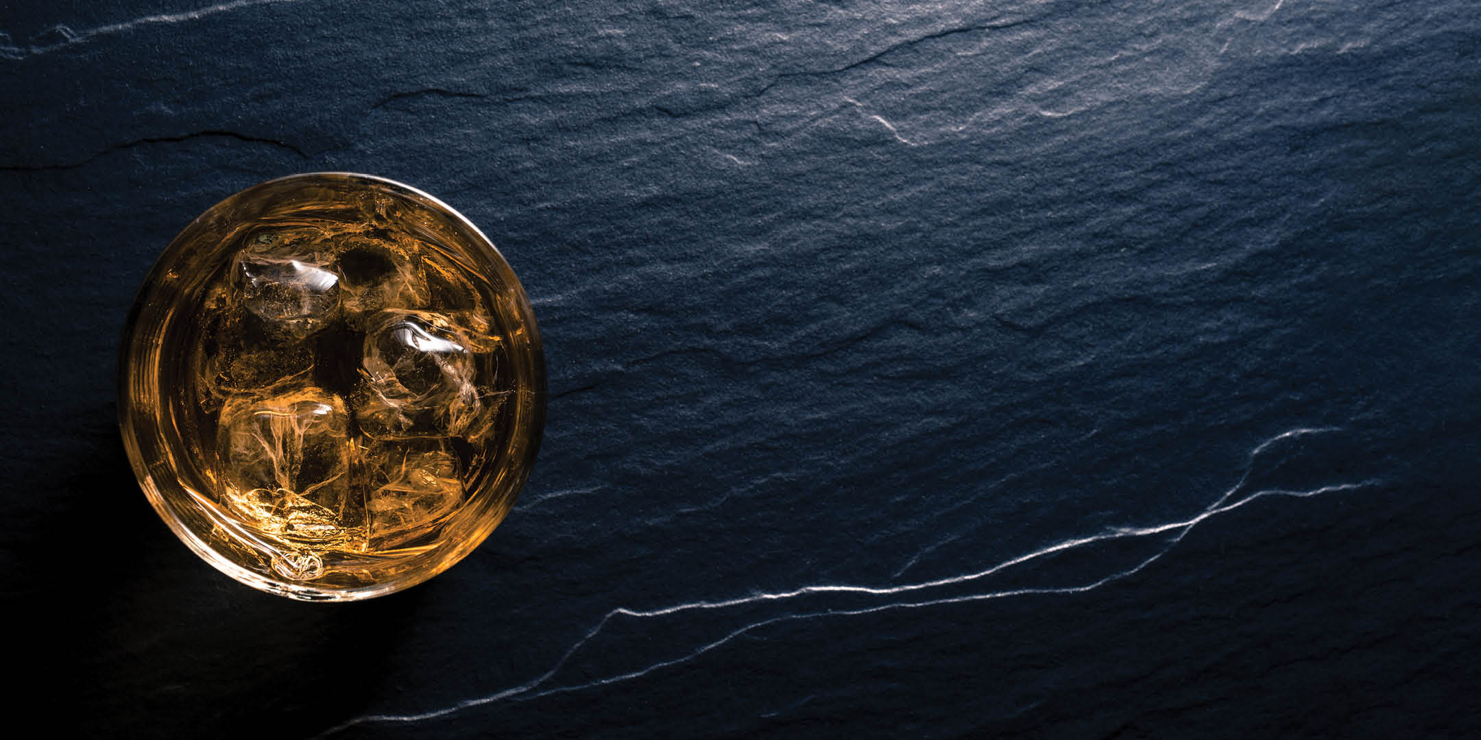 Brids-eye view of a whiskey glass on a dark grey counter.