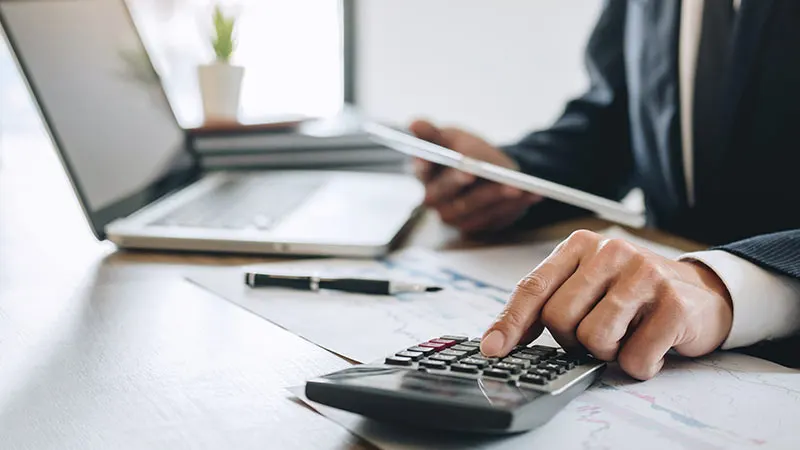 Businessman using calculator at desk with laptop