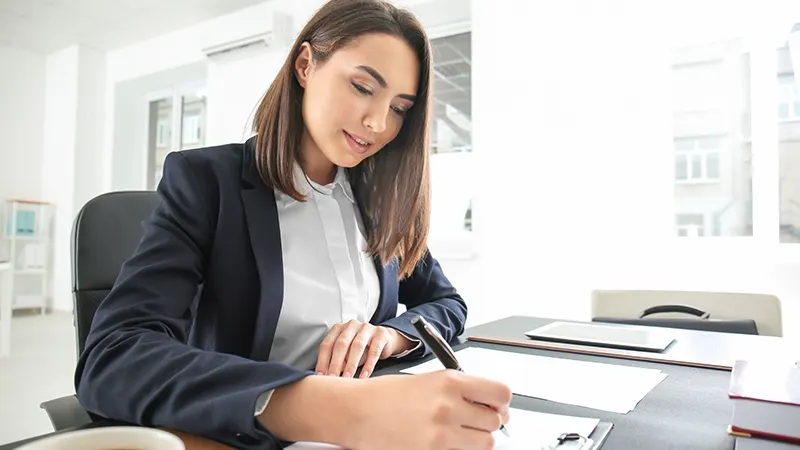 Businesswoman writing on documents at desk