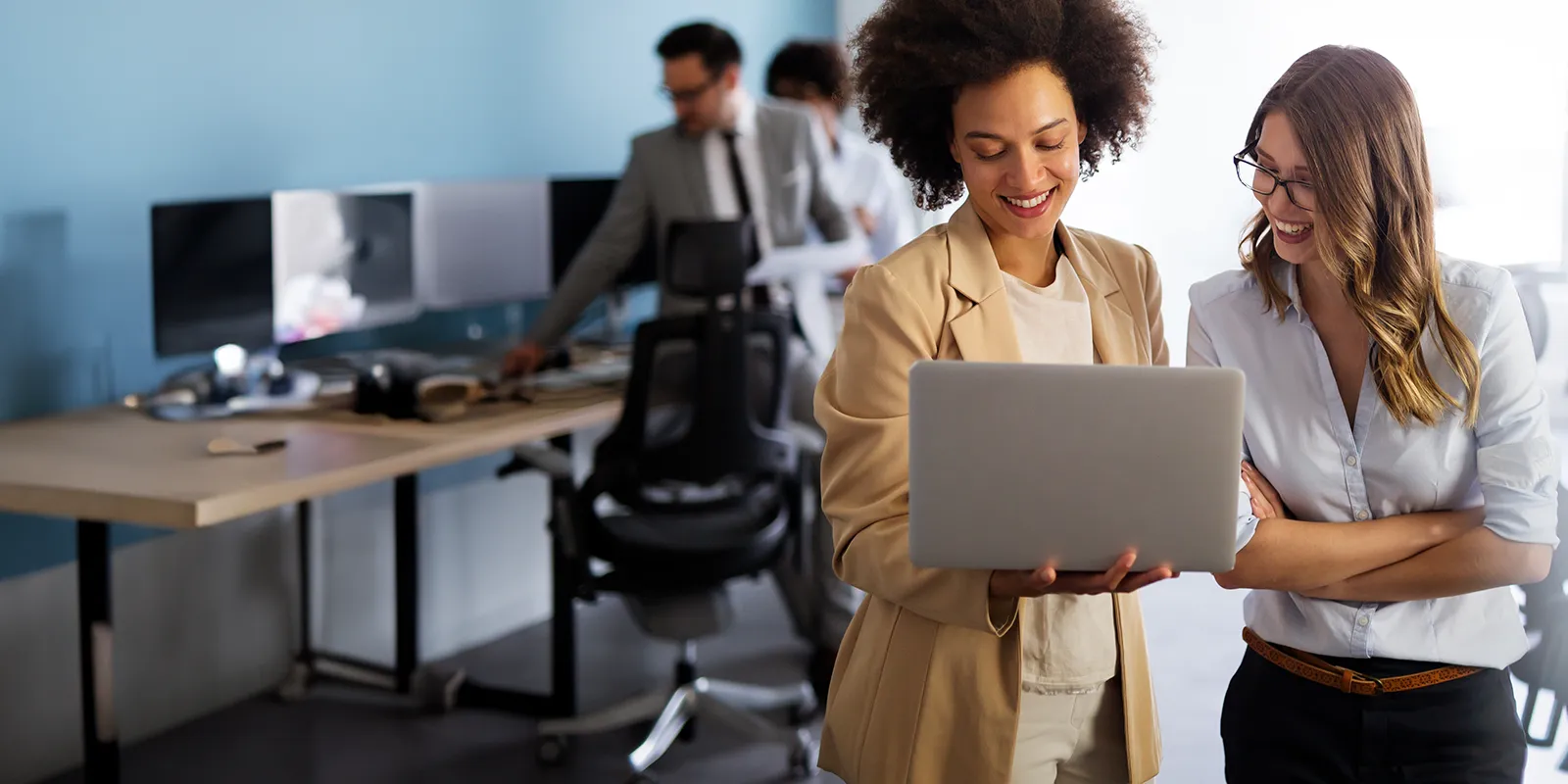 Two female office workers looking at a laptop together in a professional workplace.