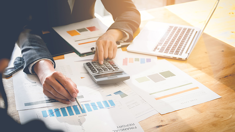 Businessperson reviewing graphs while typing on calculator