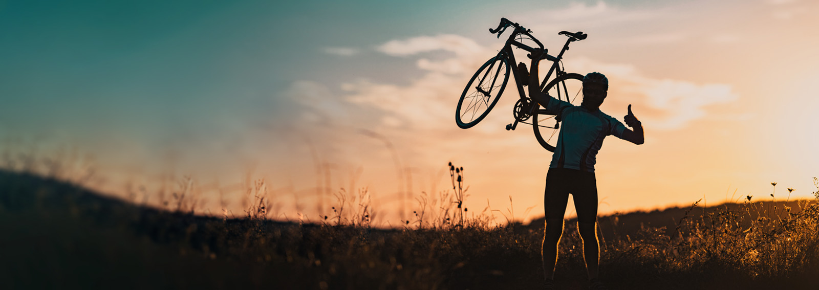 Biker holding up bike with sunset backdrop