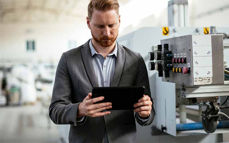 Business person reviewing tablet next to manufacturing machine