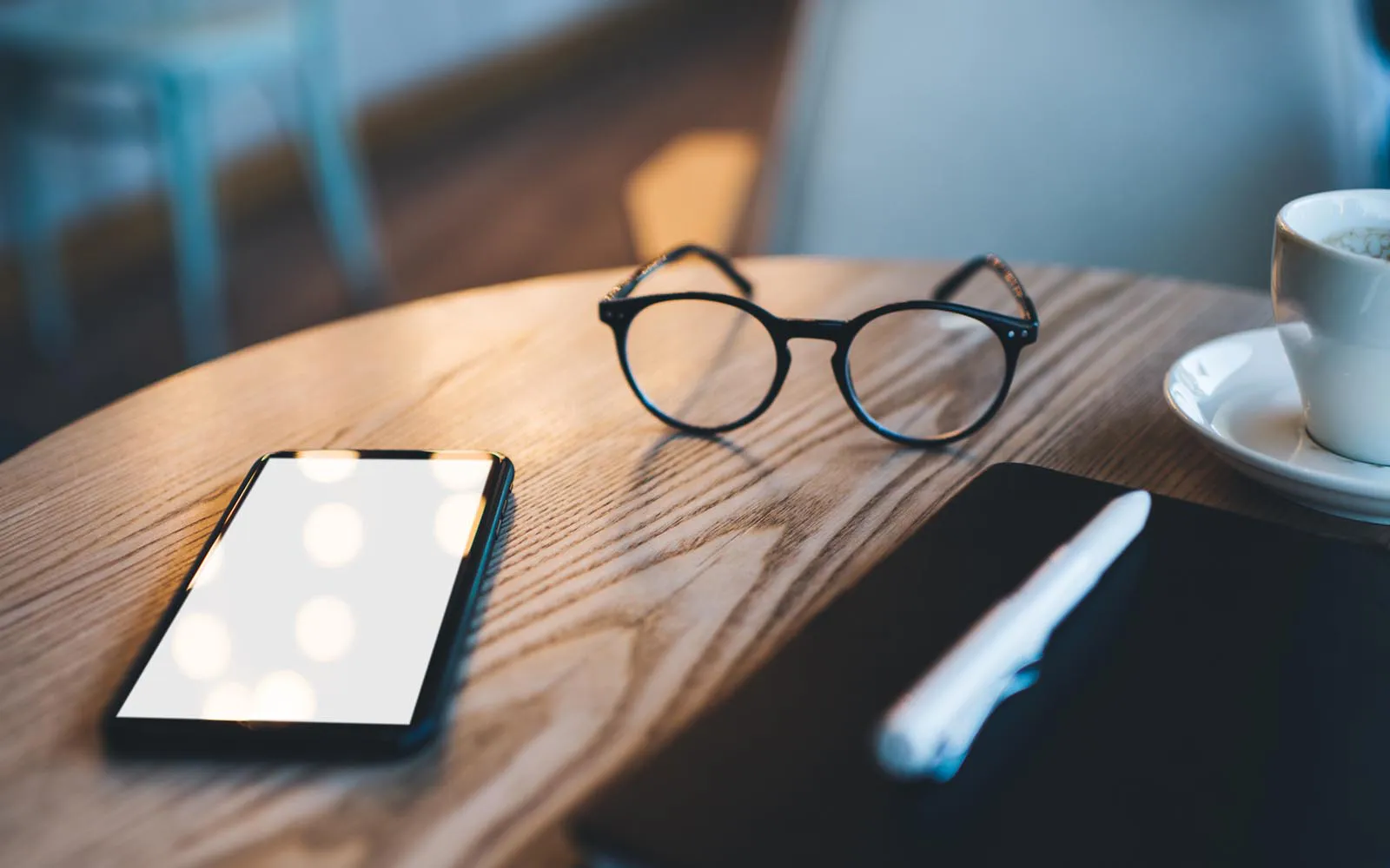 A pair of glasses, a phone and a notebook on a table